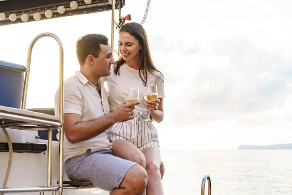 Young loving couple sitting on the yacht deck and drinking wine — Stock Photo, Image