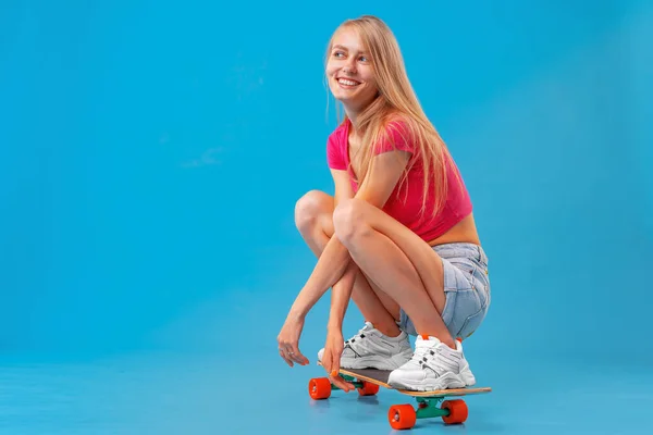 Bella donna felice vestita con disinvoltura si siede sul suo skateboard — Foto Stock