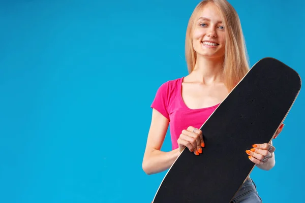 Attraente giovane donna che tiene il suo skateboard su sfondo blu — Foto Stock