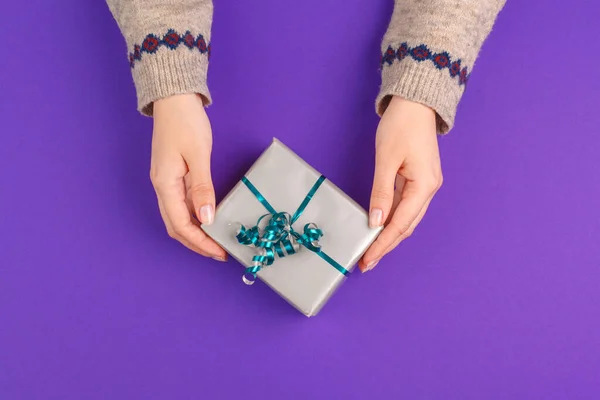 Les mains féminines tenant cadeau enveloppé sur fond violet — Photo