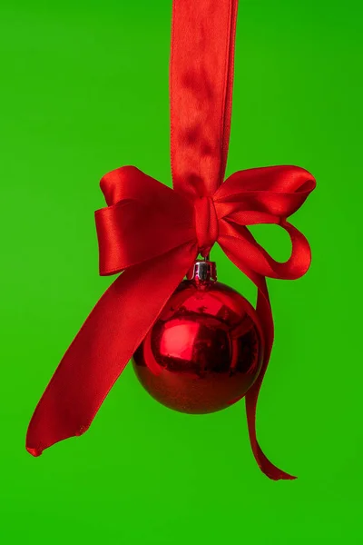 Świąteczna bombka wisząca na czerwonej satynowej wstążce na zielonym tle — Zdjęcie stockowe