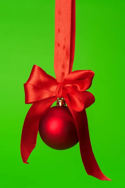 Świąteczna bombka wisząca na czerwonej satynowej wstążce na zielonym tle — Zdjęcie stockowe