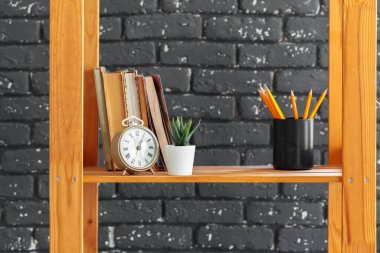 Kara tuğla duvara karşı kitap ve ıvır zıvır dolu ahşap bir kitaplık.