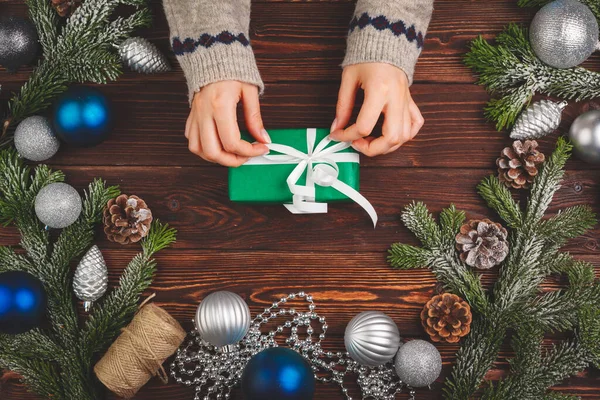 Dekoracje świąteczne na drewnianym stole z ozdobionym prezentem w rękach kobiet — Zdjęcie stockowe