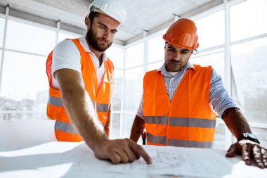 İnşaat alanındaki masada proje planına bakan iki mühendis.