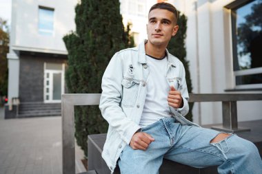 Sokakta tek başına merdivenlerde oturan sıradan bir genç.