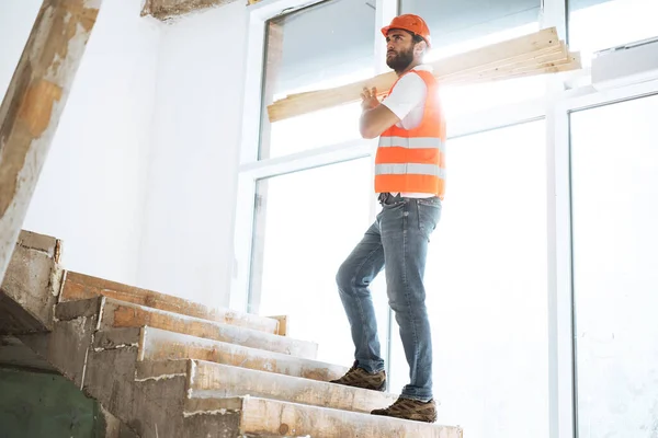 Byggare man i hatt transporterar timmer på byggarbetsplatsen, närbild . — Stockfoto