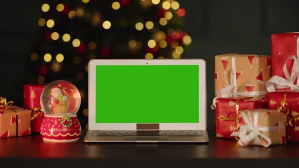 Φορητός υπολογιστής με πράσινη οθόνη στο τραπέζι με χριστουγεννιάτικα στολίδια κατά χριστουγεννιάτικο δέντρο — Αρχείο Βίντεο