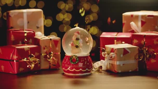 Schneekugel und Weihnachtsgeschenke auf dem Tisch — Stockvideo