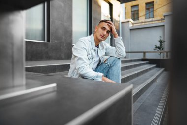 Sokakta tek başına merdivenlerde oturan sıradan bir genç.