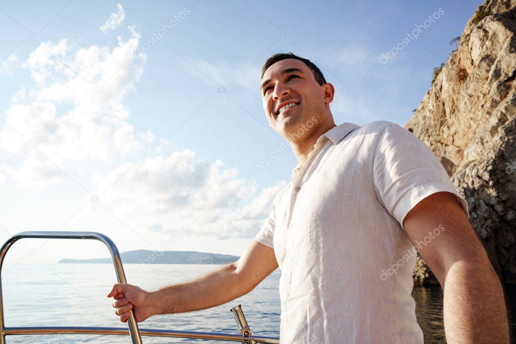 Young man in white shirt standing on the nose yacht in the sea