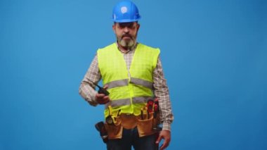 Kıdemli inşaatçı stüdyoda mavi arka planda telsiz kullanıyor.