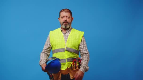 Sorrindo homem sênior construtor em colete e hardhat contra fundo azul — Vídeo de Stock
