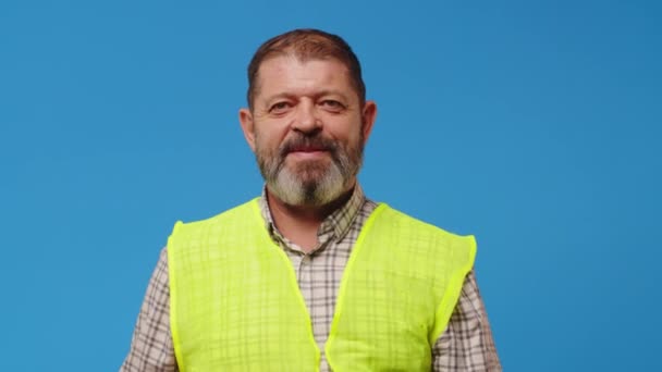 Usmívající se starší muž stavitel v vestě a hardhat na modrém pozadí — Stock video