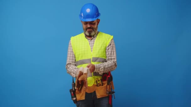 Kıdemli inşaatçı mavi arka plana karşı koruyucu eldivenler giyer. — Stok video