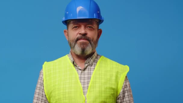 Lachende senior man bouwer in vest en hardhat tegen blauwe achtergrond — Stockvideo
