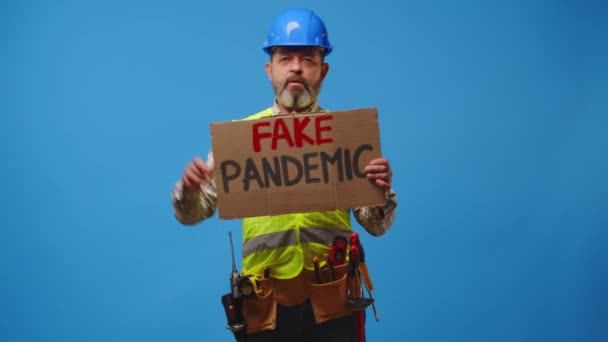 Senior man builder in hardhat holding cardboard placard striking against blue background — Stock video