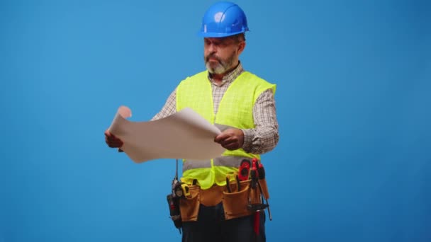 Senior Mann Baumeister in Hardhat Blick auf Baupläne vor blauem Hintergrund — Stockvideo