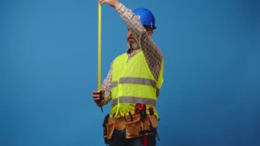 Kıdemli inşaatçı mavi arka planda mezura kullanıyor.