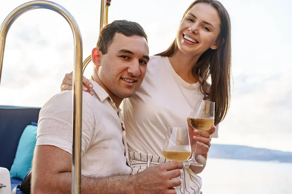Jovem casal amoroso sentado no convés do iate e beber vinho — Fotografia de Stock