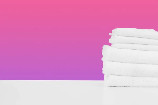 Stacked clean towels on white table against color background — Stock Photo, Image
