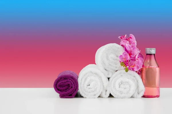 Pilha de toalhas brancas e garrafas de cuidados com a pele na mesa branca — Fotografia de Stock