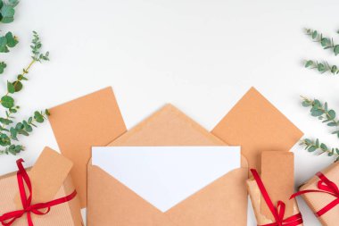 Kırmızı fiyonklu bir Noel hediyesi ve beyaz ahşap arka planda tebrik kartı.