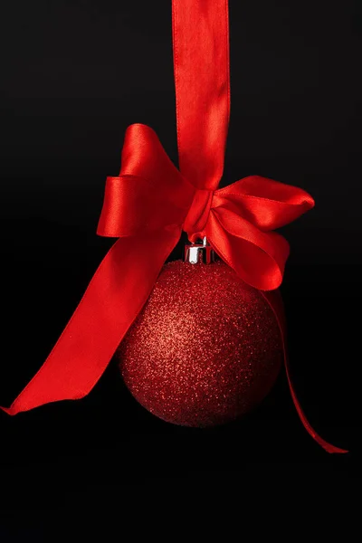 Bola de Navidad colgando en cinta de satén rojo sobre fondo negro — Foto de Stock