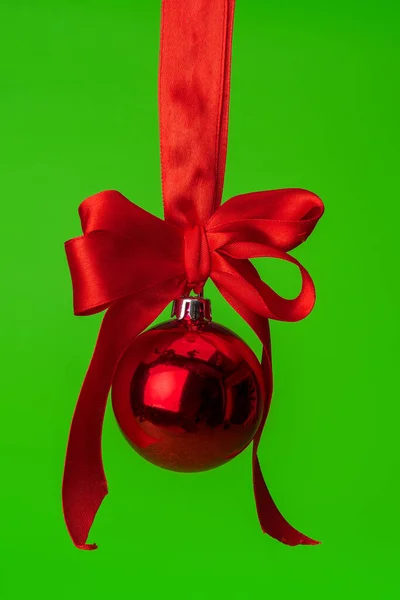 Weihnachtskugel hängt auf rotem Satinband vor grünem Hintergrund — Stockfoto
