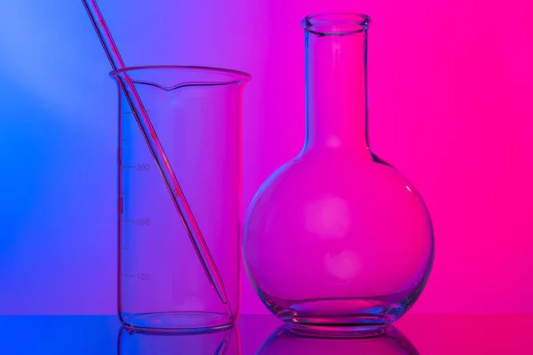 Хімічний скляний посуд крупним планом на неоновому рожево-фіолетовому фоні — стокове фото