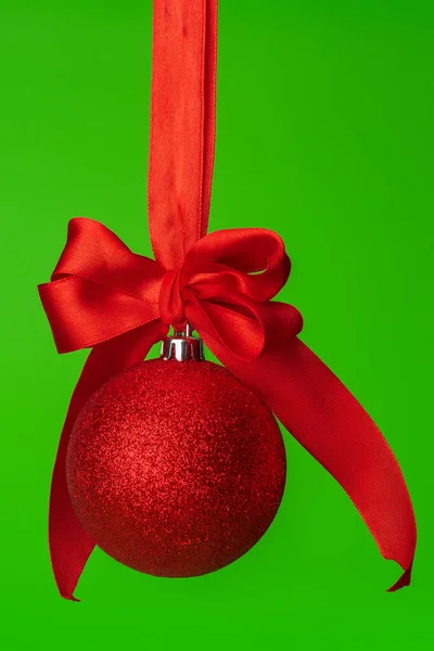 Vánoční cetka visí na červené saténové stuze proti zelenému pozadí — Stock fotografie