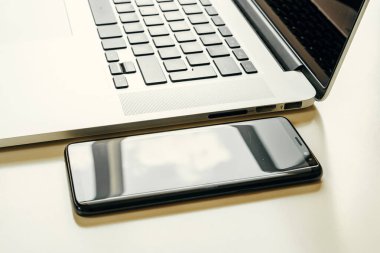 Açık dizüstü bilgisayarın yanındaki siyah akıllı telefonu kapat