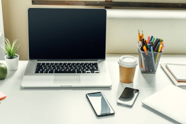 Ofis malzemeleriyle birlikte çalışma masasında bir ışık odasında dizüstü bilgisayar.
