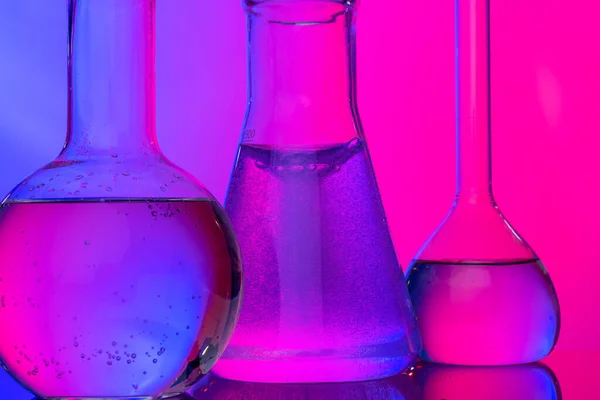 Chemical glassware close up on neon pink-purple background — Stock Photo, Image