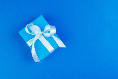 Mavi arka planda fiyonk ile süslenmiş hediye kutusunun düzlüğü