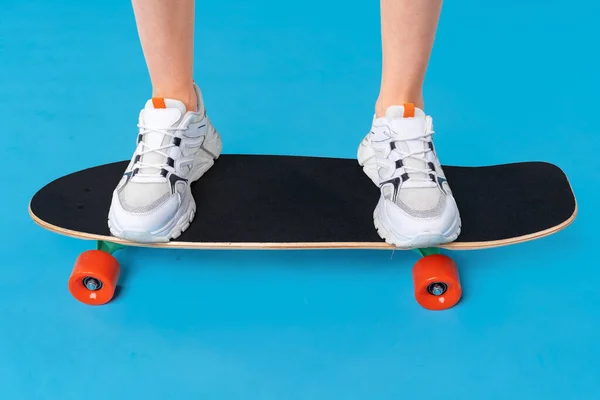 Teenager girl standing and posing on skateboard over a color background — Stock Photo, Image