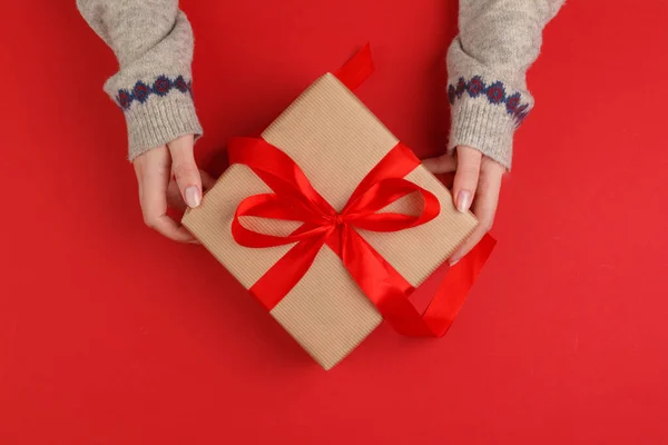 Manos femeninas con regalo de Navidad sobre fondo rojo, vista superior, espacio para copiar — Foto de Stock