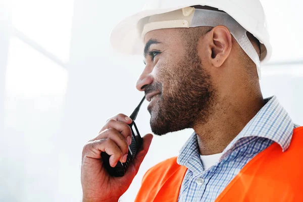 Jovem trabalhador da construção em uniforme usando walkie talkie no local — Fotografia de Stock