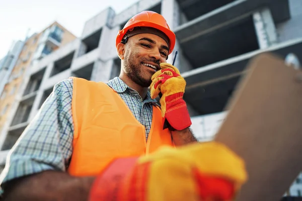 Jovem trabalhador da construção em uniforme usando walkie talkie no local — Fotografia de Stock
