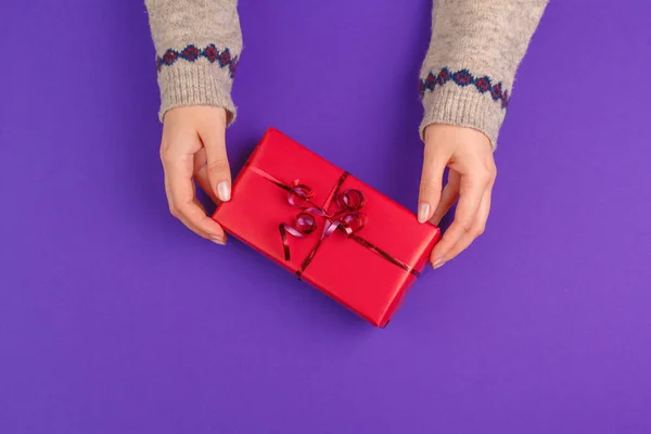 Les mains féminines tenant cadeau enveloppé sur fond violet — Photo