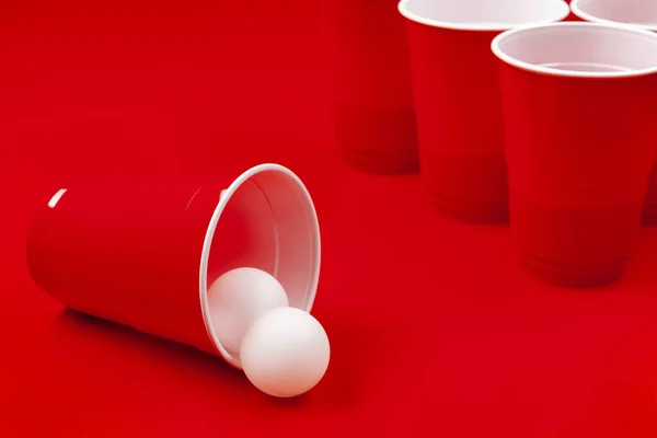 Tazze e palla di plastica su sfondo rosso. Birra pong gioco — Foto Stock