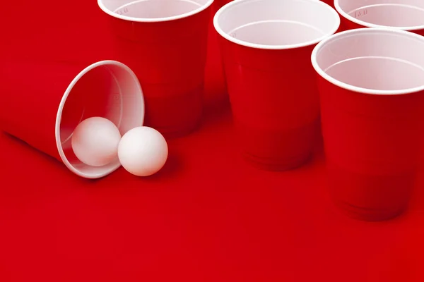 Copas y bola de plástico sobre fondo rojo. Cerveza pong juego — Foto de Stock