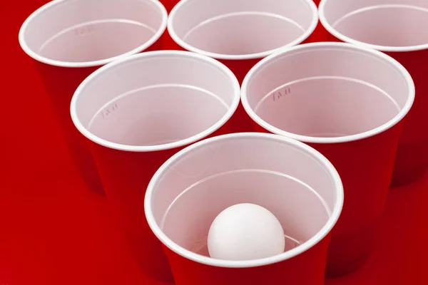 Tasses et boule en plastique sur fond rouge. Jeu de Bière Pong — Photo