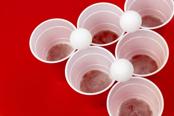 Κούπες και πλαστική μπάλα σε κόκκινο φόντο. Παιχνίδι μπύρα πονγκ — Φωτογραφία Αρχείου