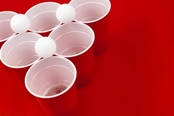 Copos e bola de plástico no fundo vermelho. Jogo de pong de cerveja — Fotografia de Stock