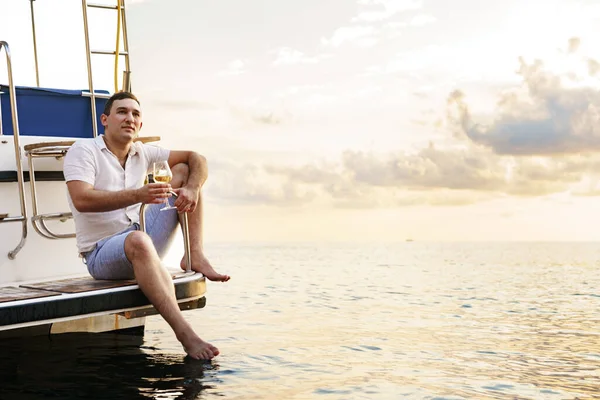 Young man holding a glass of wine on an open deck of a cruise boat — Stock Photo, Image