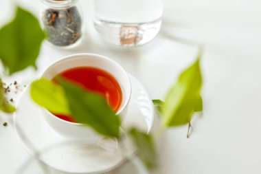 Kuru çay kavanozuyla beyaz masada bir fincan sıcak siyah çay.