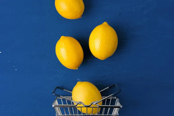 전형적 인 파란색 배경의 쇼핑 카트에 있는 레몬, 맨 위에 보이는 것 — 스톡 사진