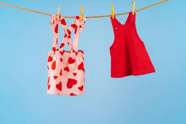 Baby meisje kleding vastgepind op een waslijn tegen blauwe achtergrond — Stockfoto