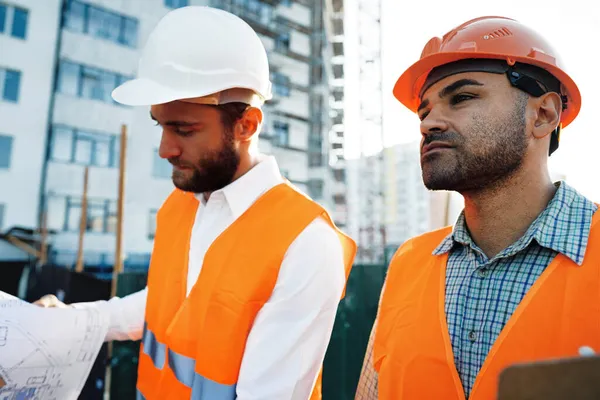 Två unga manliga ingenjörer i uniform och hatt arbetar på byggarbetsplatsen — Stockfoto